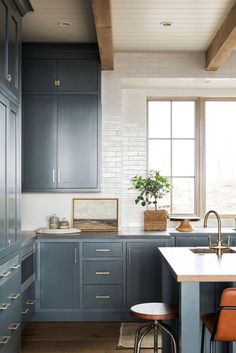 a kitchen with blue cabinets and stools next to a counter top in front of a window