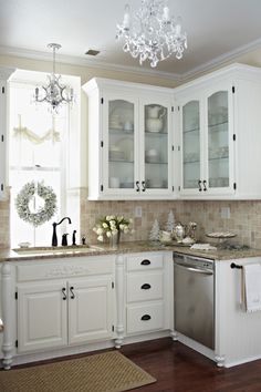 a kitchen with white cabinets and marble counter tops, chandelier above the dishwasher