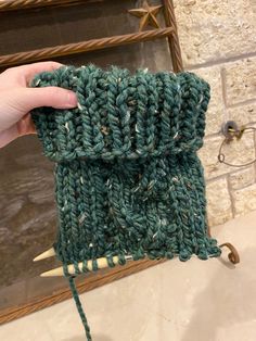 someone is holding up a green knitted pouch