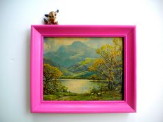 a pink frame with a painting on it and a small stuffed animal in the corner