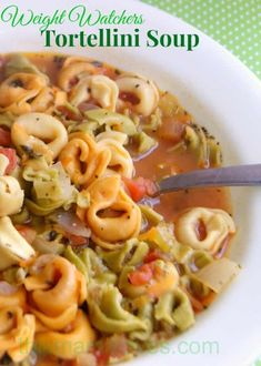 a white bowl filled with tortellini soup on top of a green table cloth