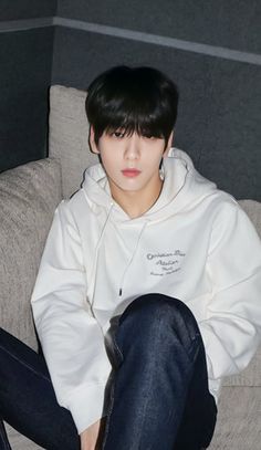 a young man sitting on top of a couch wearing jeans and a white hoodie