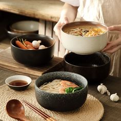 a woman holding a bowl of noodles with shrimp and carrots