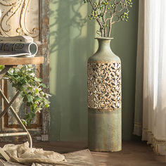 a green vase with flowers in it sitting on a table next to a bookcase