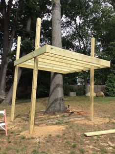 a wooden structure sitting in the middle of a yard next to a tree and some chairs