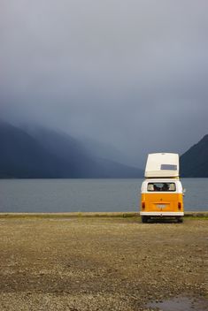 an orange and white camper van parked on the side of a body of water