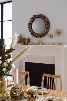 a dining room table is set with gold plates and place settings in front of a fireplace