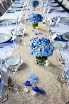 a long table is set with blue and white flowers in glass vases, silverware, and napkins