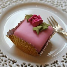 a pink frosted cake with a rose on top sits on a plate next to a fork