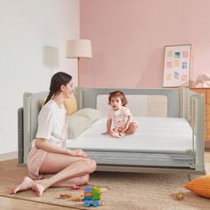 a woman sitting on the floor next to a child's bed with a toddler in it