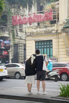 two people are standing on the sidewalk in front of a building