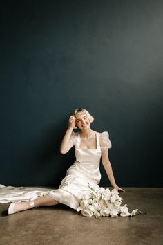 a woman sitting on the floor with flowers in her hair and wearing a white dress