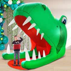 a young boy standing in front of a large green alligator balloon with its mouth open