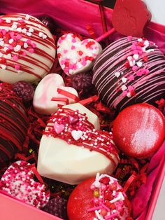 a pink box filled with lots of different types of heart shaped chocolates and sprinkles