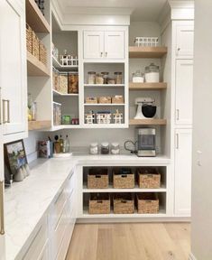 a kitchen with white cabinets and lots of baskets on the counter top in front of it