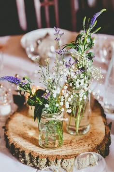 flowers in mason jars are placed on a wood slice at the center of a table