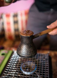 a person is holding a wooden spoon over a small metal container with something in it