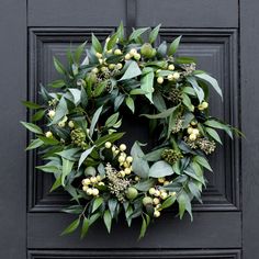 a wreath is hanging on a door with green leaves and berries around it's edges