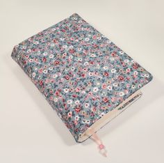 an open book with flowers on it sitting on a white table next to a pink cord