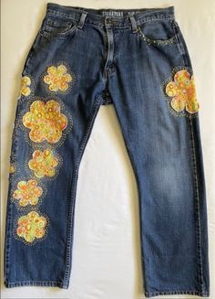 an old pair of jeans with embroidered flowers on the bottom and side, sitting on a white surface