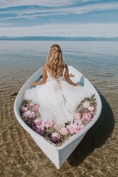 a woman in a white dress is sitting in a boat with flowers on the bottom