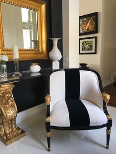 a black and white striped chair sitting in front of a mirror on a wall next to a vase