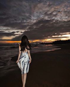 a woman is walking on the beach at sunset