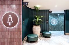 a restroom with green walls and tiled flooring has a plant in the corner next to two urinals