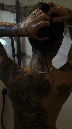 a man with tattoos on his back and arms is looking at himself in the mirror