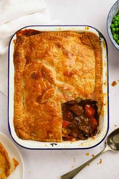 a casserole dish with meat and vegetables in it on a table next to peas