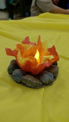 a lit candle sitting on top of some rocks and paper in the shape of a flower