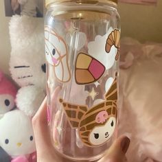 a person holding a glass cup with cartoon stickers on the lid and in front of some stuffed animals