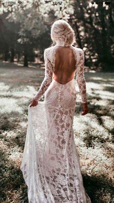 a woman in a white dress is walking through the grass with her back to the camera