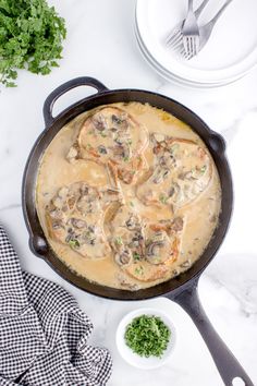 a skillet filled with food on top of a counter next to plates and utensils