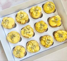 twelve yellow cupcakes in a white box with silver decorations on the top and sides