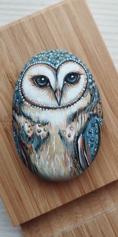 an owl painted on a rock sitting on top of a wooden board next to a piece of wood