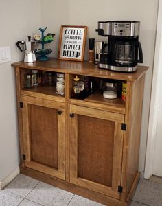 a small wooden cabinet with coffee maker and other items on the top, next to a wall mounted sign