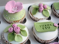 cupcakes decorated with fondant flowers and green leaves are displayed in a box