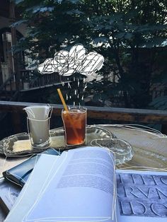 an open book sitting on top of a table next to two glasses and a drink