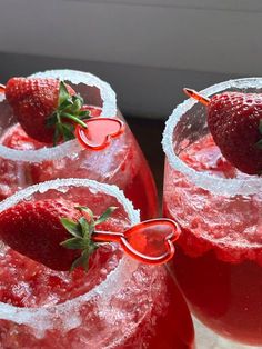 three glasses filled with red liquid and strawberries on the rims, sitting next to each other