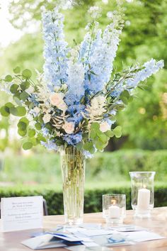 a vase filled with blue and white flowers on top of a table next to two glasses