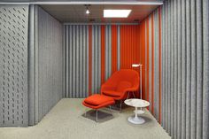 an orange chair and white table in a room with vertical striped wallpaper on the walls