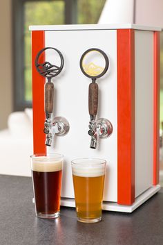 two glasses of beer sitting next to a machine with an orange and white stripe on it