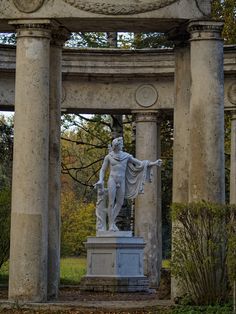 a statue in the middle of a garden with columns and arches around it, surrounded by trees