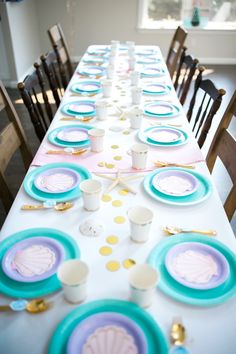 a long table with plates, cups and napkins set up for a mermaid party