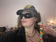 a woman wearing sunglasses and a hat with beads around her neck holding onto a necklace