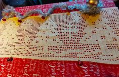 the table is covered with red and white christmas fabric, silver ornaments and tinsel