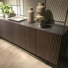 two vases are sitting on top of a wooden cabinet with metal slats behind it