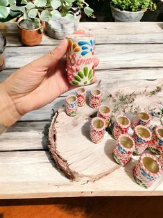 a person holding a small cup in front of some tiny cups on a wooden table