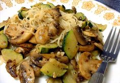 a white plate topped with noodles and vegetables next to a fork on top of a table